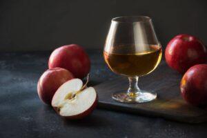 A glass of Calvados next to some apples on a wood platter, emphasizing Calvados alcohol content