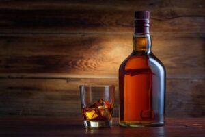 A bottle of one of Sasma's Canadian whiskys next to a rocks glass with Canadian whiskey and ice on a wooden table.