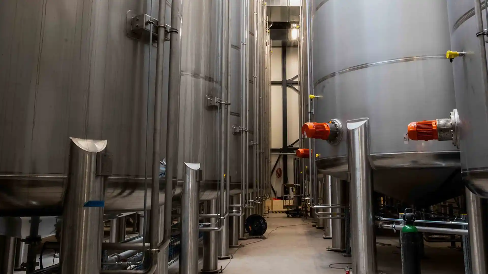 A corridor between large stainless steel tanks in an industrial facility. Pipes and valves are visible, highlighting a clean, modern setup.