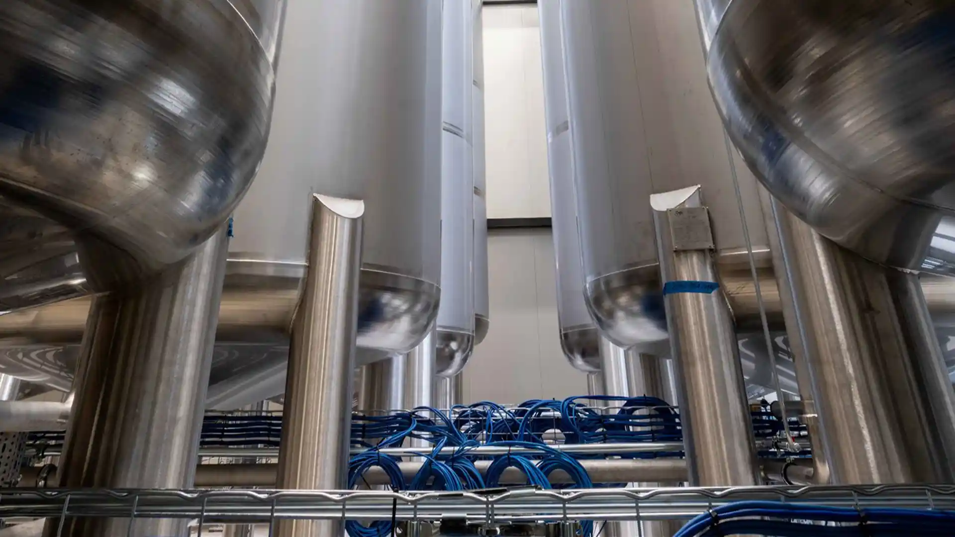 Industrial stainless steel tanks in a factory setting, with an intricate network of blue cables below, conveying a sense of precision and efficiency.