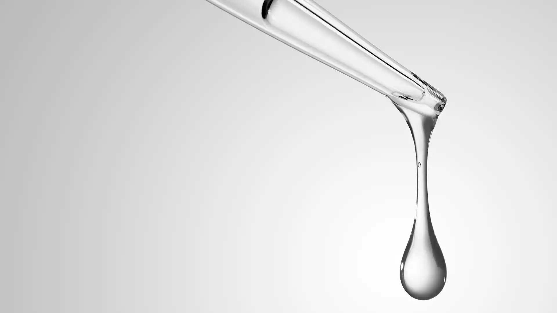A clear dropper releasing a single droplet of liquid on a plain gray background, conveying precision and purity.