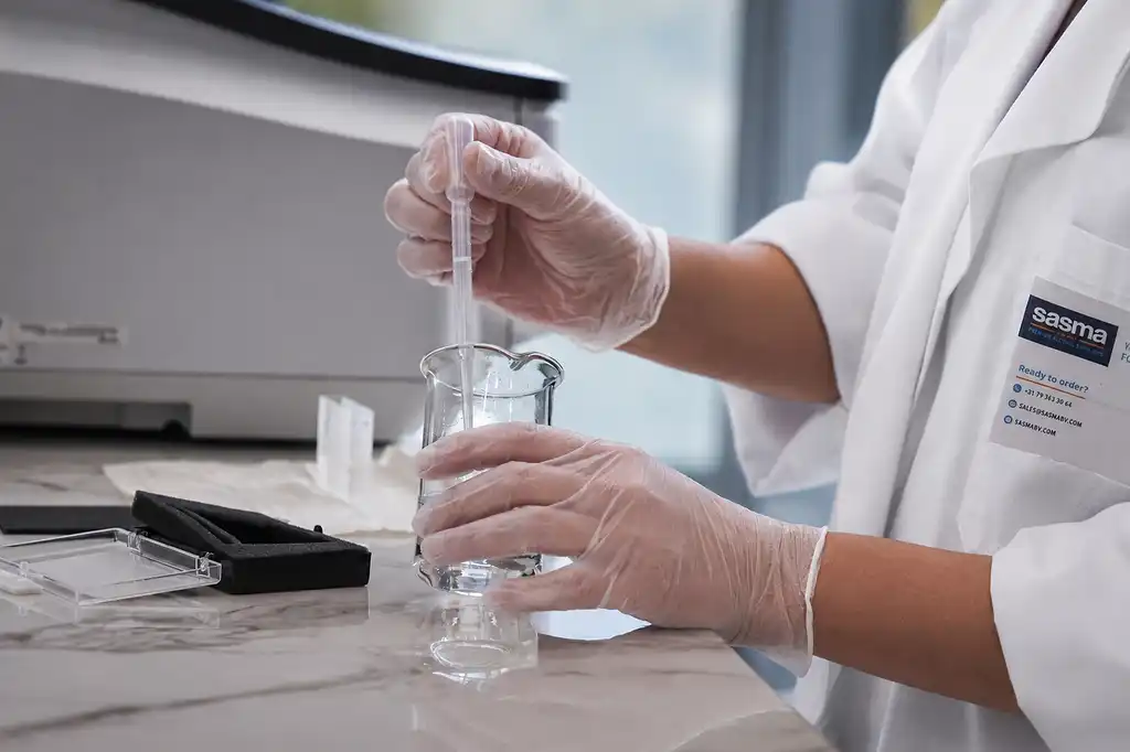 Technicien de laboratoire ganté utilisant une pipette pour transférer du liquide dans un bécher en verre, effectuant une expérience scientifique minutieuse dans un laboratoire.